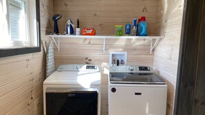 A compact laundry room with two washing machines, a drying rack, and a shelf with cleaning supplies. - Colorful Cape Cod (Lexington)