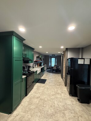 A modern kitchen with green cabinets, a black refrigerator, and a dining area with a table and chairs.