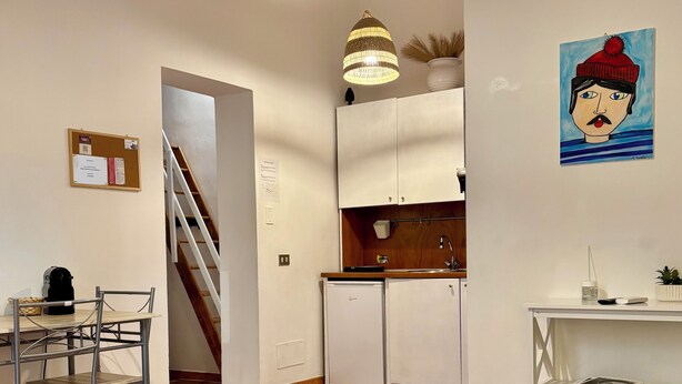 Un apartamento moderno con comedor, cocina y sala de estar. Hay una escalera que conduce a otro nivel, una mesa de comedor con sillas, un sofá y una pequeña mesa con libros.
