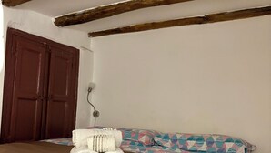 Un dormitorio con techo de madera, colcha marrón, falda de cama estampada y un juego de toallas enrolladas sobre la cama.