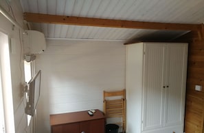A small room with a wooden ceiling, a white wardrobe, a wooden cabinet, and a chair.