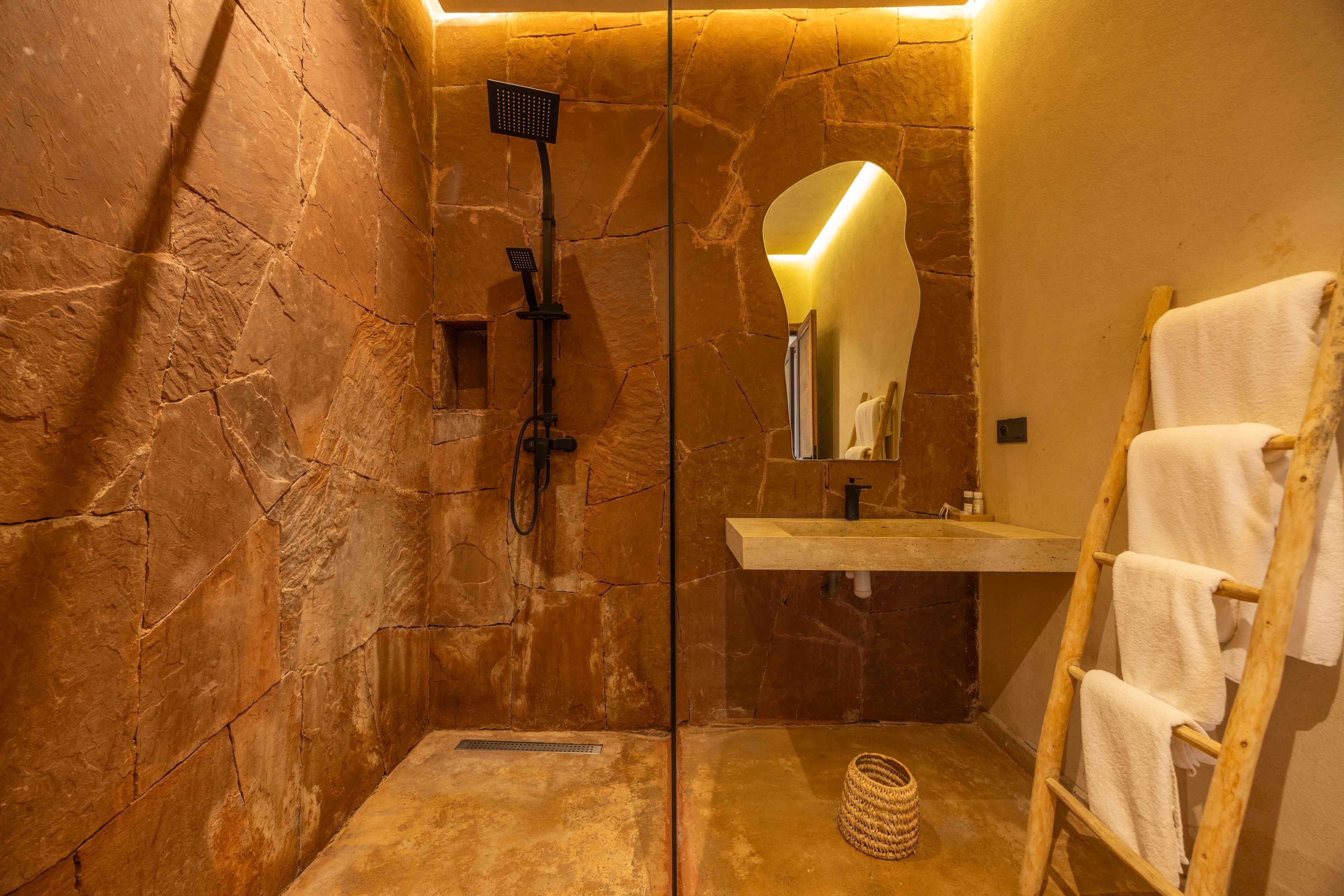 A stone-walled bathroom with a shower, a sink, a mirror, and a towel rack.