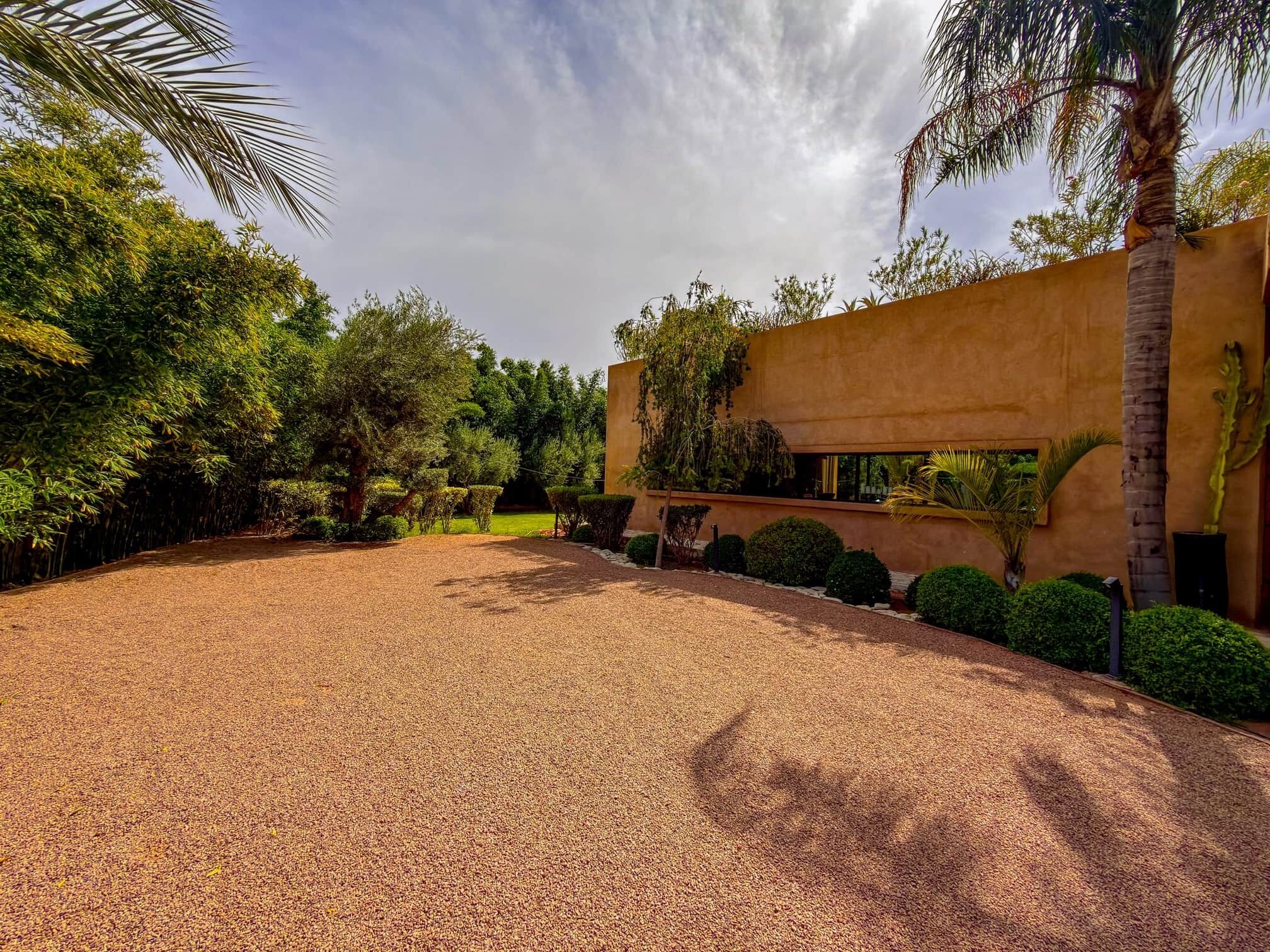 A gravel driveway leading to a building with a flat roof and a large window.