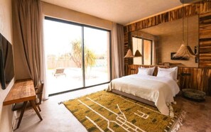 A bedroom with a bed, a desk, a large window, and a view of the outdoors.