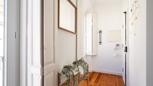 Un couloir avec un plancher en bois, des murs blancs, un miroir et une plante posée sur une étagère.