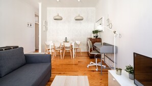 Un salon moderne avec un canapé gris, un plancher en bois, un coin repas avec des chaises blanches, une petite table et des luminaires suspendus.