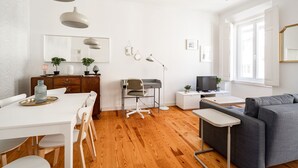 Un salon moderne avec un canapé gris, une table à manger avec des chaises, un bureau avec une chaise et un téléviseur posé sur un meuble.