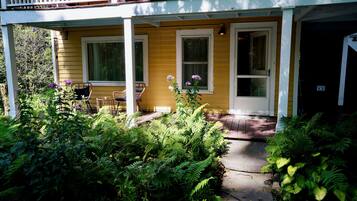 A yellow house with a porch, two windows, and a door.
