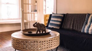 A round wooden table with a decorative elephant figurine and a small dish, placed in a living room with a dark sofa and striped cushions. - Hudson Valley Apartment in a Historic Farmhouse w/ Sauna Near Stone Ridge Hamlet (Stone Ridge)