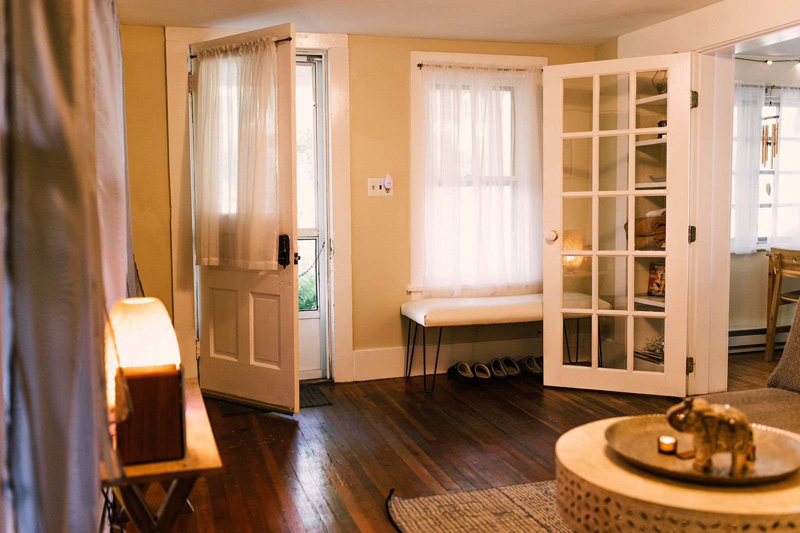 A room with a wooden floor, a bench, a door with glass panels, and a lamp.