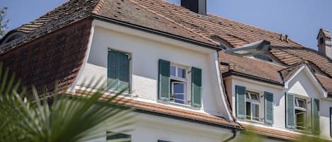 Un edificio con techo inclinado, varias ventanas con contraventanas verdes y una chimenea.