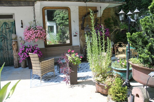 Une terrasse agrémentée de plantes en pot, d’une chaise en osier et d’un banc.