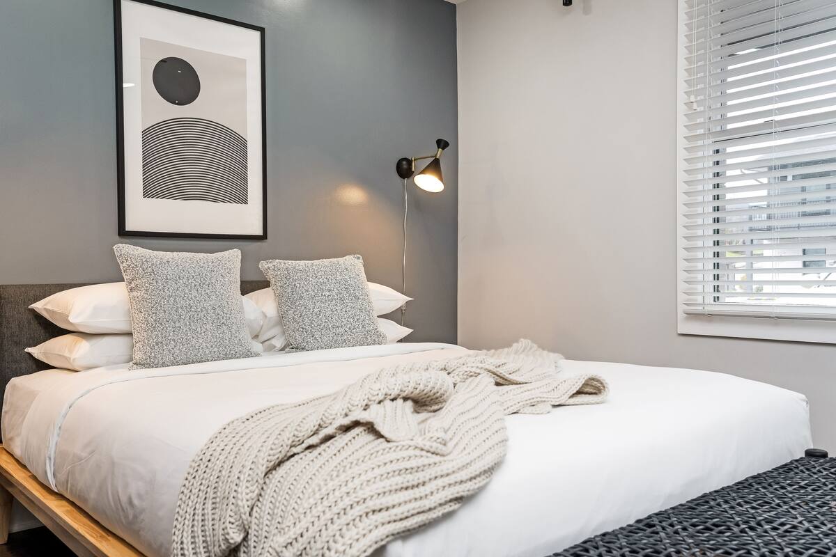 A neatly made bed with a white comforter and a knitted throw blanket.