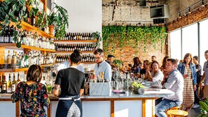 A bar area with a brick wall, wooden bar counter, and shelves of bottles. - Abode Nashville - Germantown (Nashville)