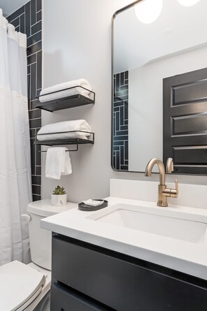 Un baño moderno con un lavamanos blanco, un grifo dorado y un perchero negro.