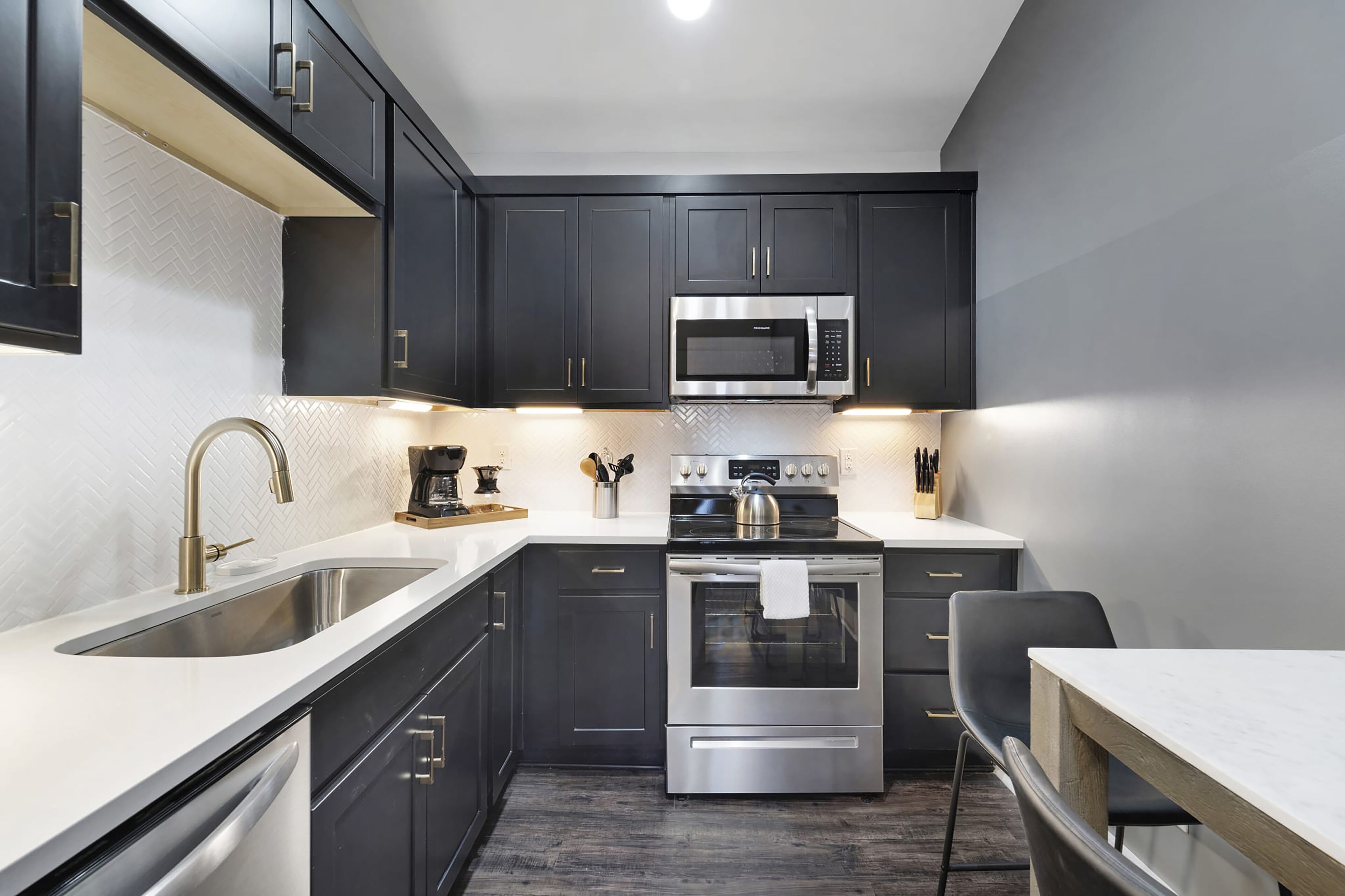 A modern kitchen with dark cabinets, a stainless steel microwave, an oven, and a sink.
