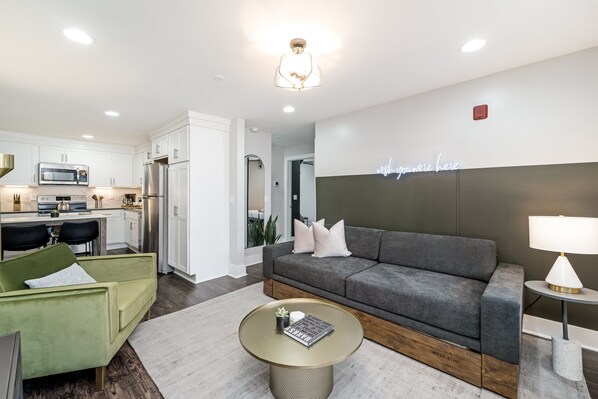 Una sala de estar moderna con un sofá gris, un sillón verde y una mesa de centro redonda.