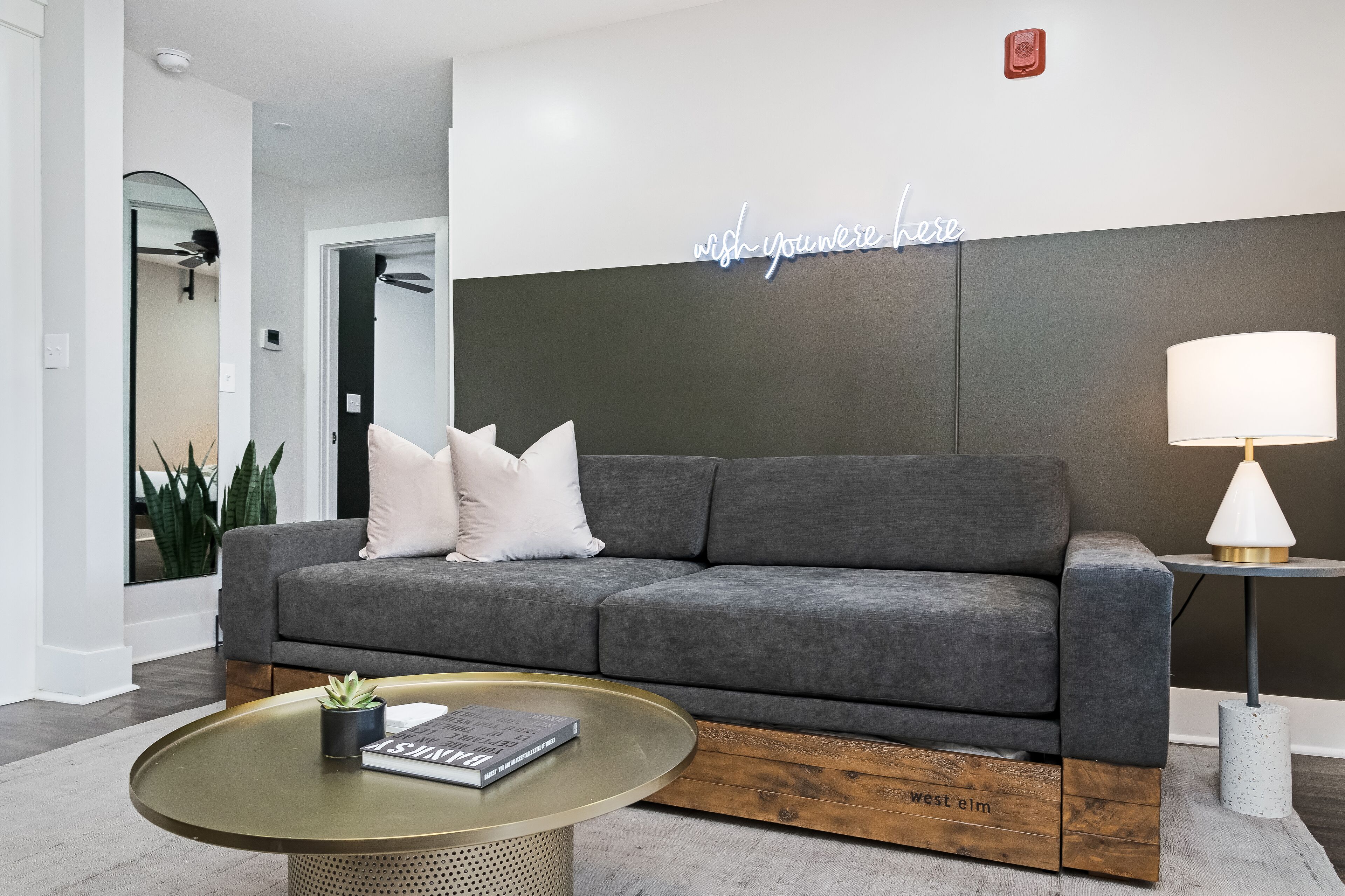 Un salon moderne avec un canapé gris, une table basse en verre et une petite table d’appoint sur laquelle se trouve une lampe.