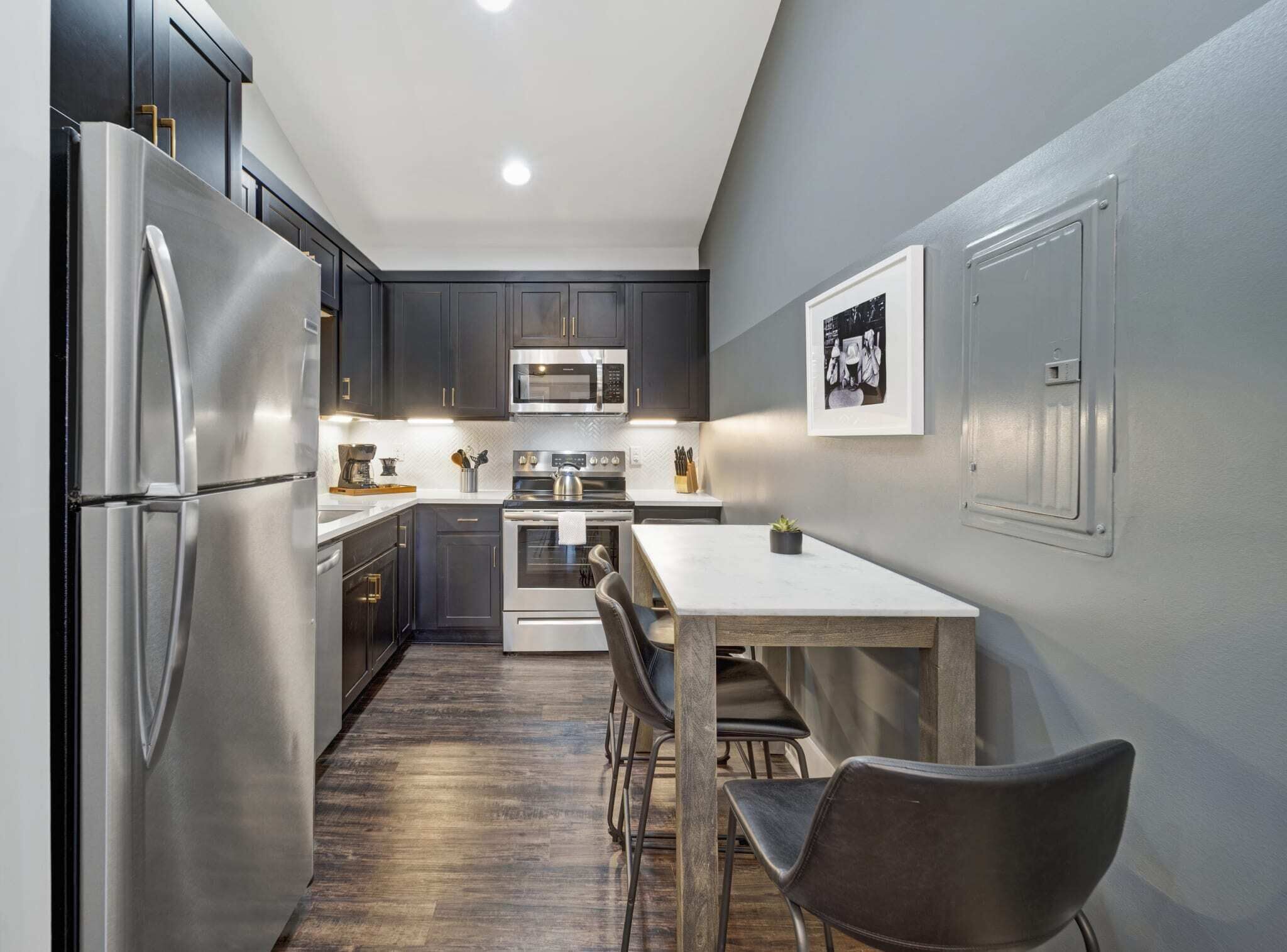 A modern kitchen with dark cabinets, stainless steel appliances, and a wooden dining table.
