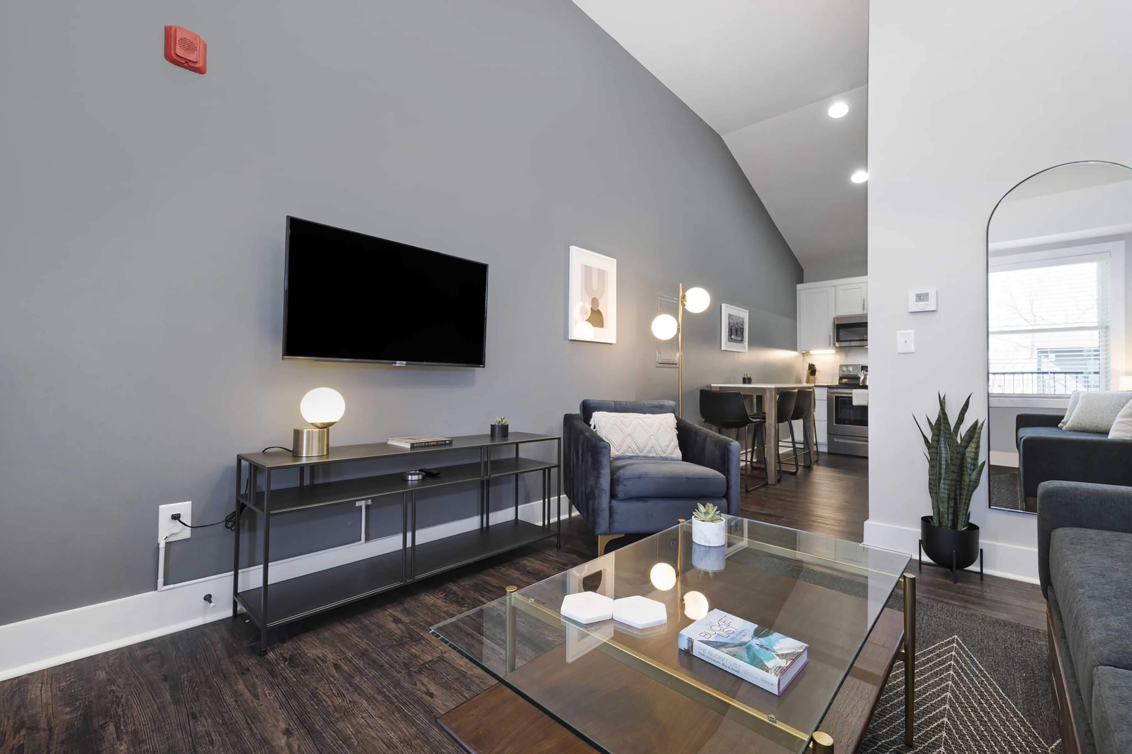 Een moderne woonkamer met een flatscreen televisie, een glazen salontafel en een donkergrijze bank.