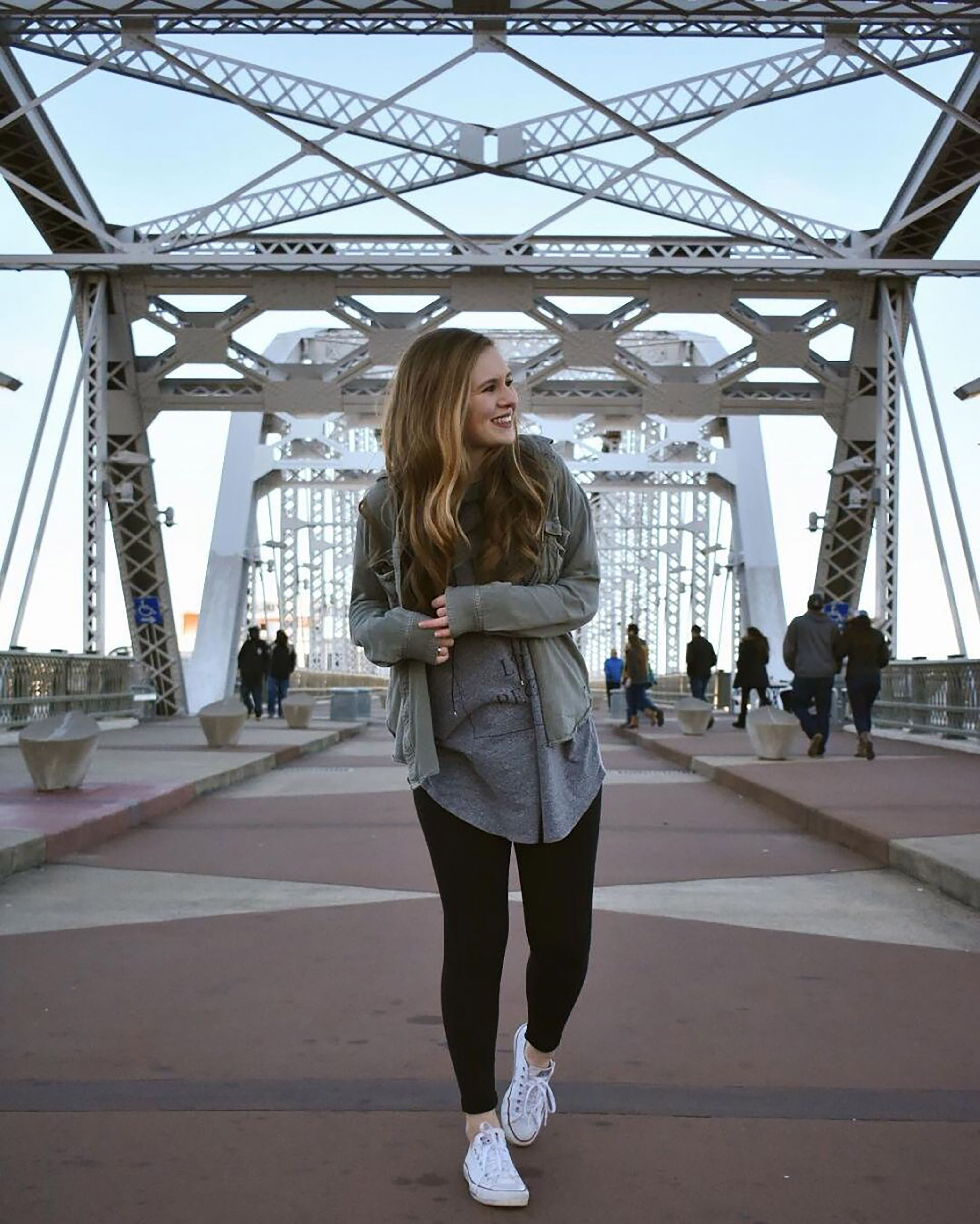 Une personne se tient sur un pont piétonnier doté d’une structure métallique et de panneaux de verre.