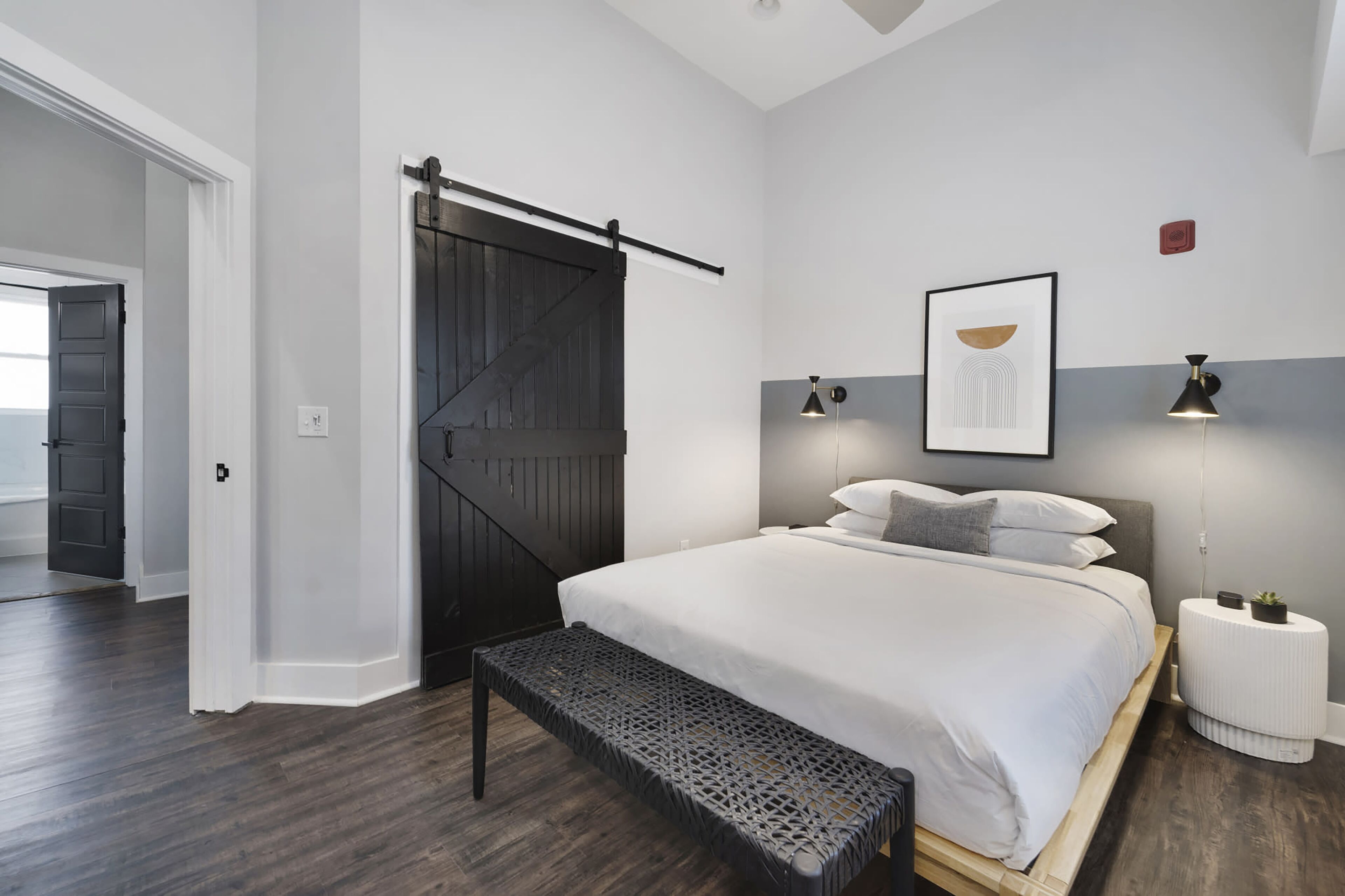 A bedroom with a large bed, a bench, a sliding door, and a bedside table with a lamp.