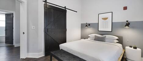 Un dormitorio con una cama grande, un banco, una puerta corredera y una mesita de noche con una lámpara.