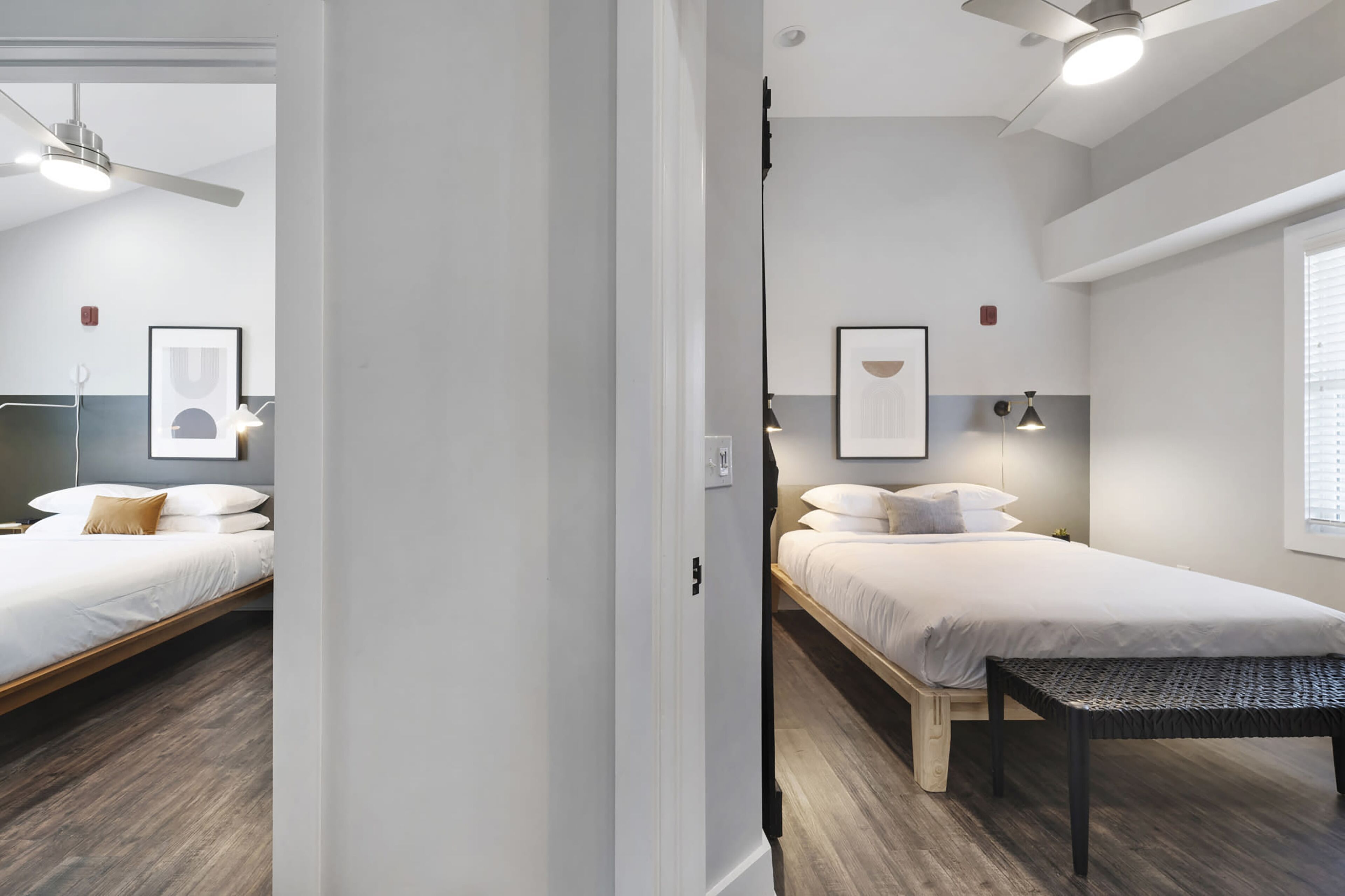 A modern hotel room with two single beds, a wooden bench, and a ceiling fan.