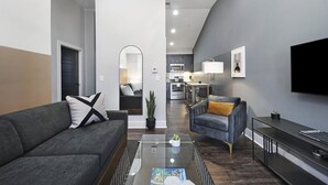 A modern living room with a gray sofa, a blue armchair, a coffee table, and a flat-screen TV mounted on the wall. - Abode Nashville - Germantown (Nashville)