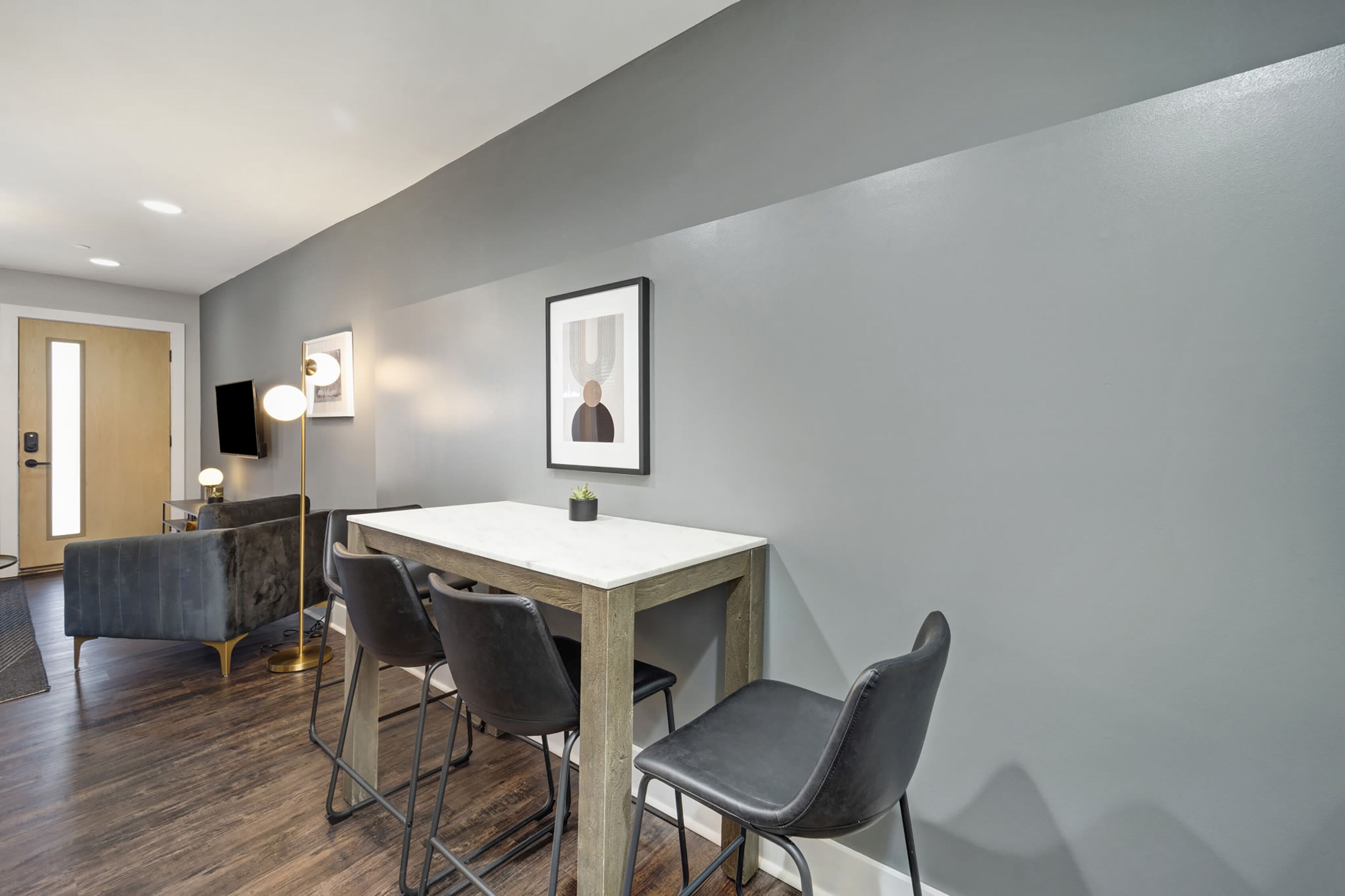 A modern dining area with a wooden table, black chairs, and a grey wall.