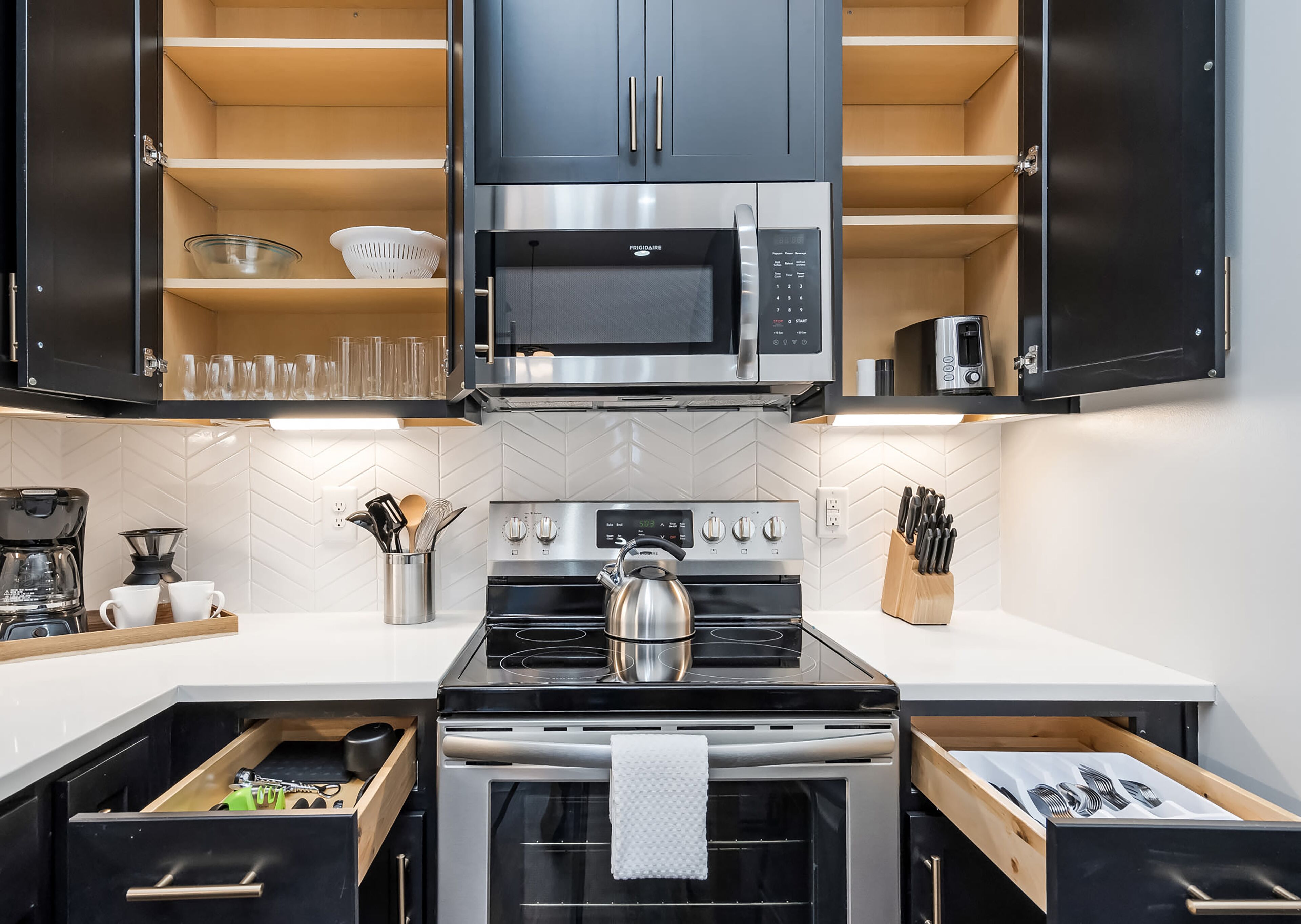 Una cocina moderna con armarios negros, estufa de acero inoxidable, microondas y tetera.