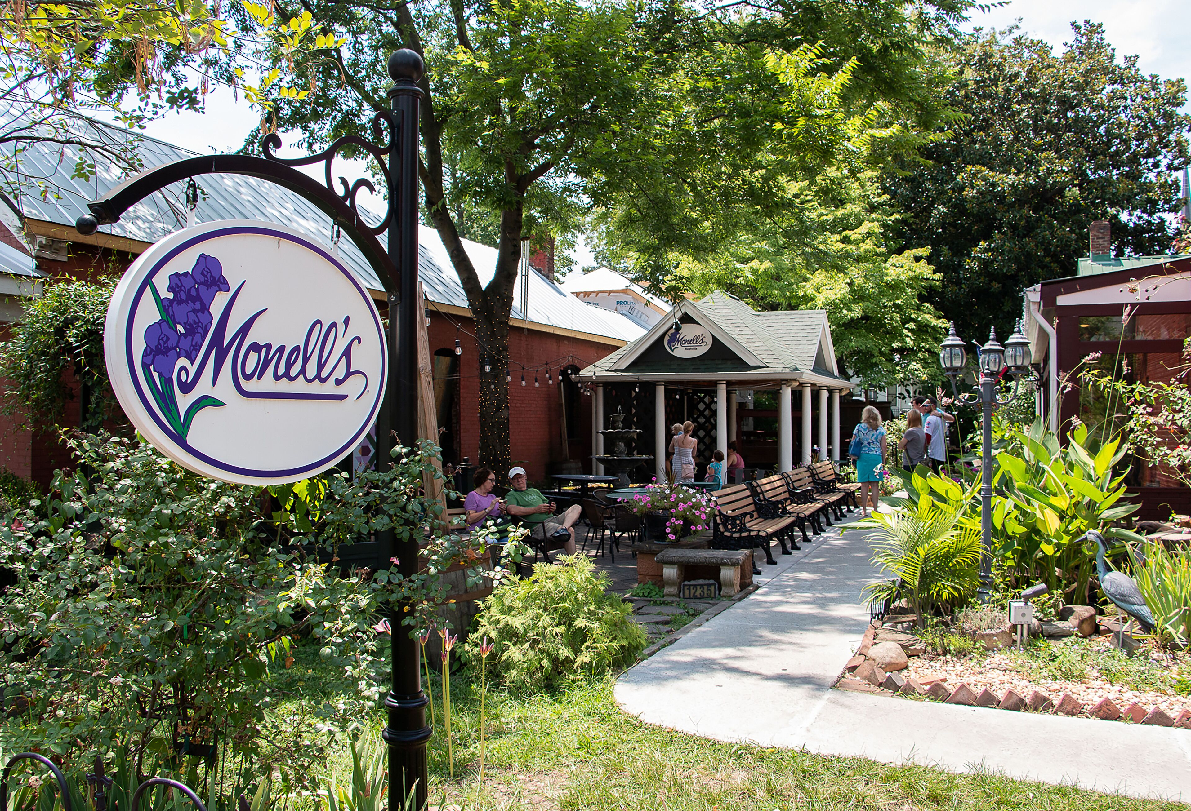 A restaurant named Monelli's with outdoor seating, surrounded by greenery and a pathway.