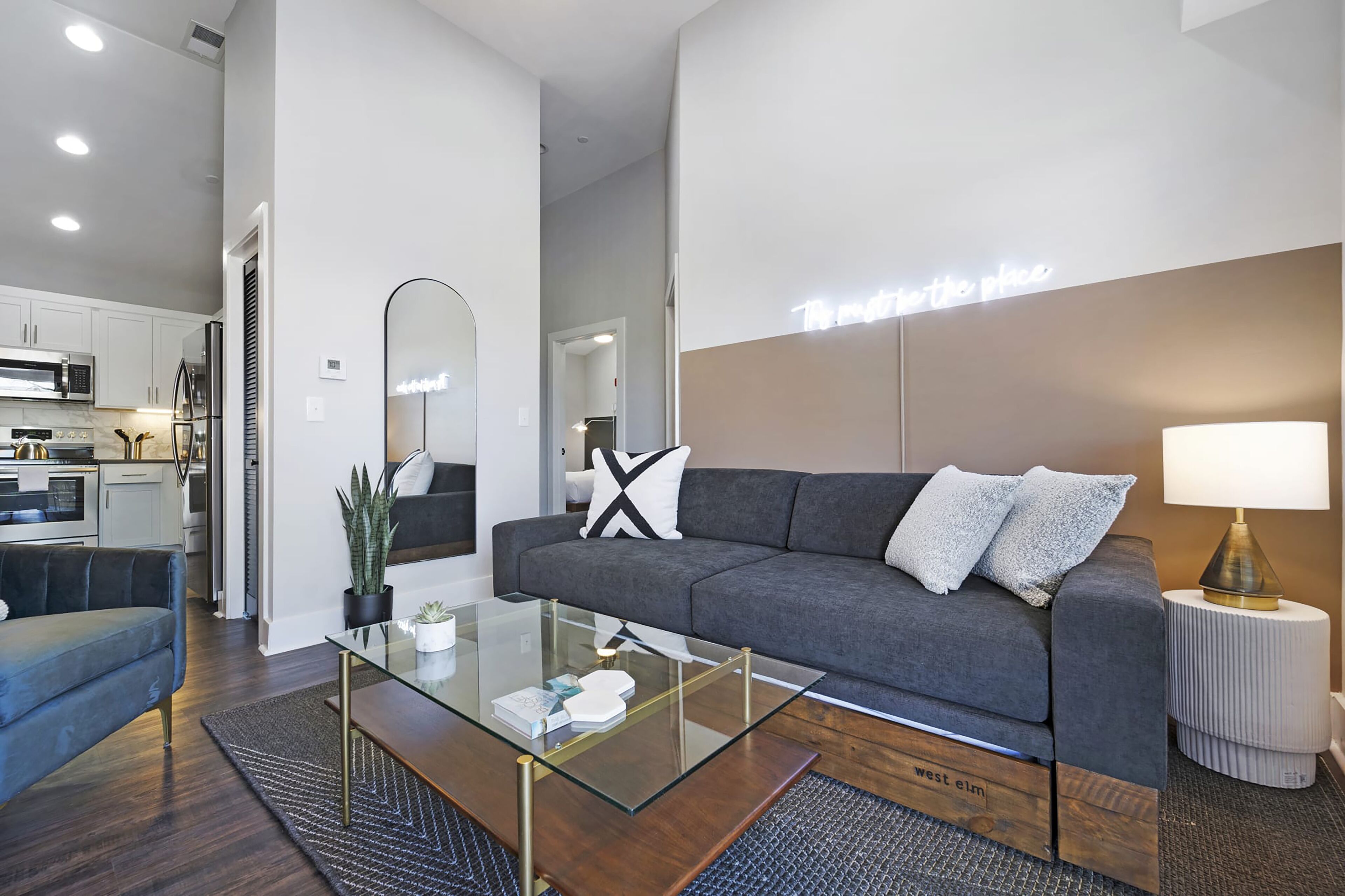 A modern living room with a grey sofa, a glass coffee table, and a small side table with a lamp.