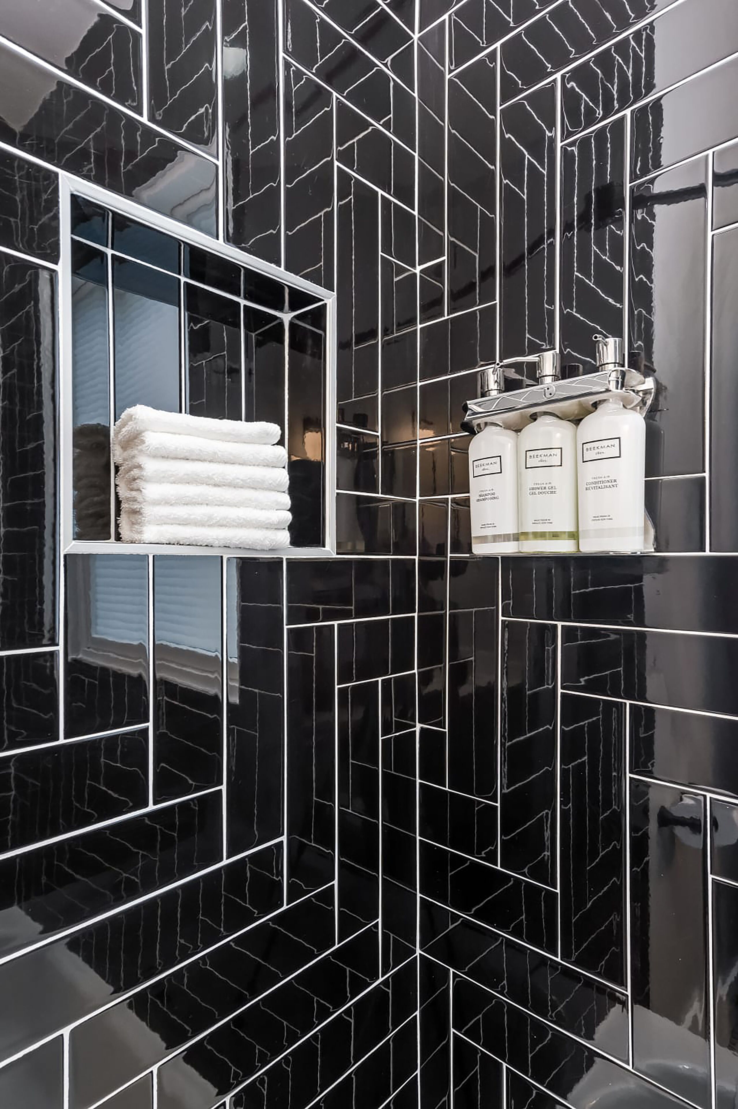 A bathroom with black marble tiles, a window with a towel rack, and three bottles of Schwarzkopf shampoo and conditioner.