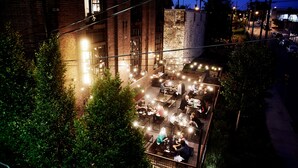 An outdoor dining area with string lights and tables, surrounded by greenery and a brick building. - Abode Nashville - Germantown (Nashville)