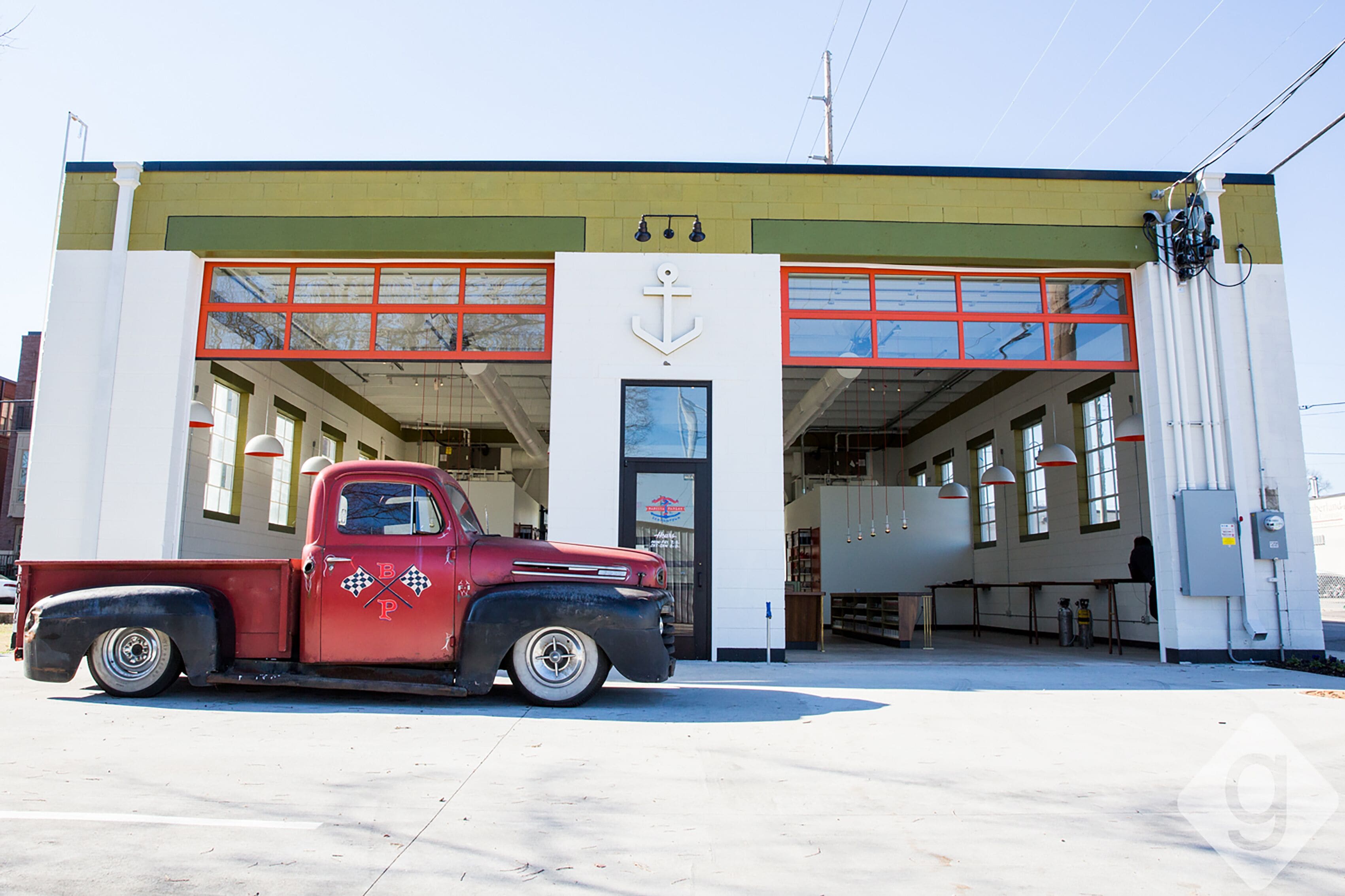 A vintage red truck parked in front of a building with a white facade and red-framed windows.