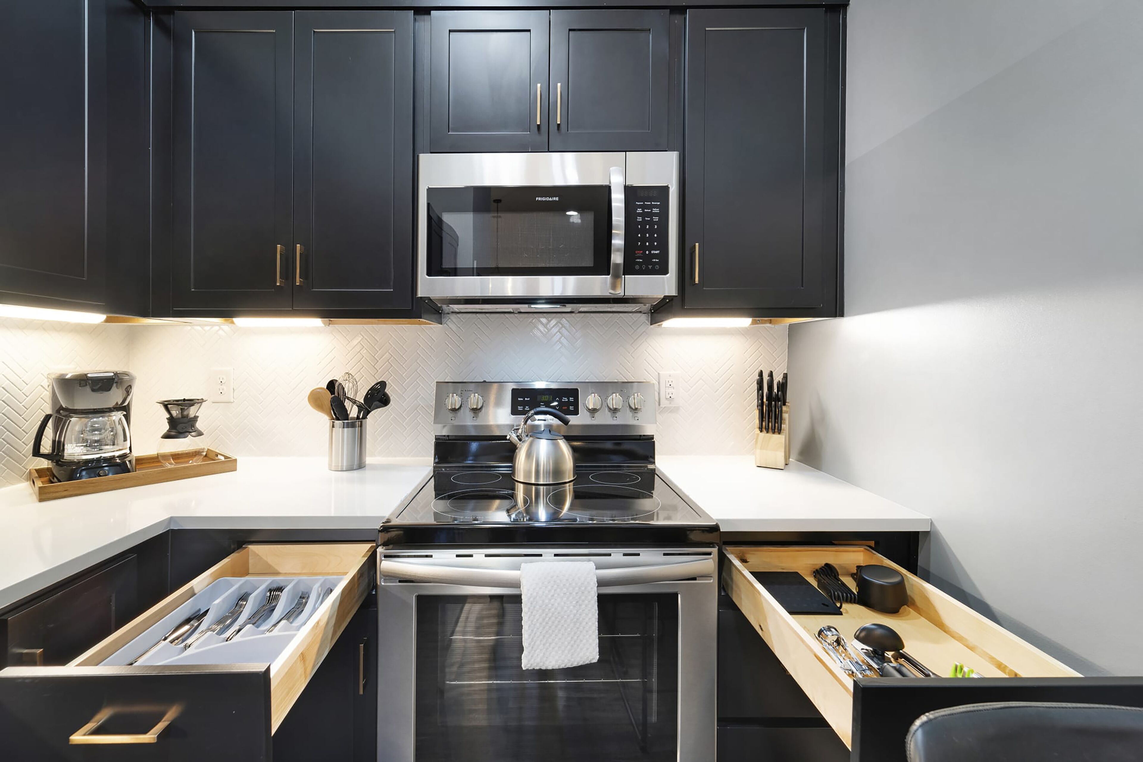 Een moderne keuken met donkere kastjes, een roestvrijstalen magnetron, een gasfornuis en een inbouwoven.