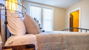 A bedroom with a bed, a nightstand, a lamp, and a window with blinds.