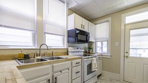 A kitchen with white cabinets, a stainless steel sink, a microwave, and a stove.