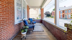 A covered porch with brick walls, two wicker chairs, a small table, and potted plants.