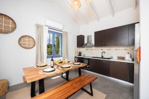 A modern kitchen with dark cabinets, a wooden dining table set for four, and a large window with curtains.