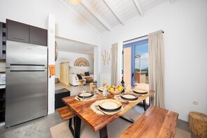 A modern kitchen with a stainless steel refrigerator, a dining table set with plates, glasses, and a fruit bowl.