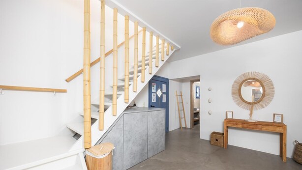 Un interior moderno con una escalera, una consola con espejo y una lámpara colgante.