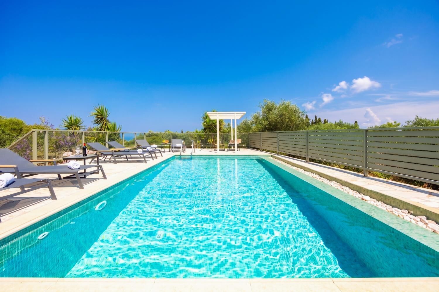 Une piscine rectangulaire à l’eau d’un bleu cristallin, entourée de chaises longues et agrémentée d’une pergola.