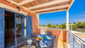 Un balcón con una mesa dispuesta para comer, una puerta que da a una habitación interior y vistas del paisaje circundante.
