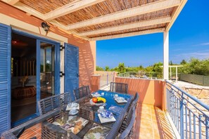 Un balcon avec une table dressée pour le dîner, une porte donnant sur une pièce intérieure et une vue sur le paysage environnant.