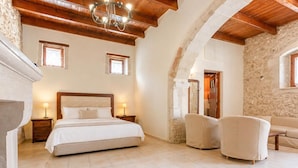 Ein Schlafzimmer mit einem großen Bett, zwei Nachttischen, einer Kandelaber, einer Steinwand und einem Durchgang zu einem anderen Raum.