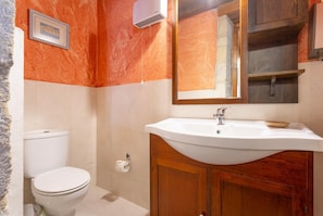 Un baño con lavamanos blanco, armarios de madera, un inodoro y un espejo.