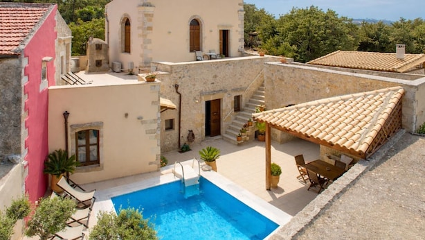 Eine Villa mit Swimmingpool, Sitzgelegenheiten im Freien und einer Stein-Fassade.
