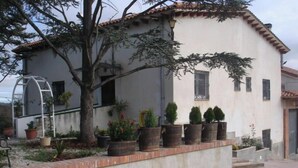 Un bâtiment à deux étages, doté d’un toit en tuiles, d’un petit porche agrémenté de plantes en pot et d’un chemin en béton menant à l’entrée.